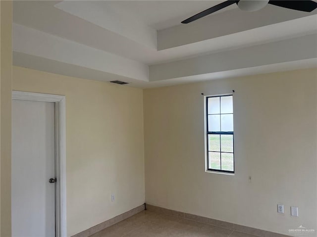 spare room with a tray ceiling, light tile patterned floors, visible vents, ceiling fan, and baseboards