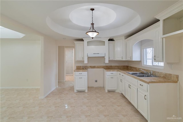 kitchen with pendant lighting, light tile patterned floors, a raised ceiling, a sink, and under cabinet range hood