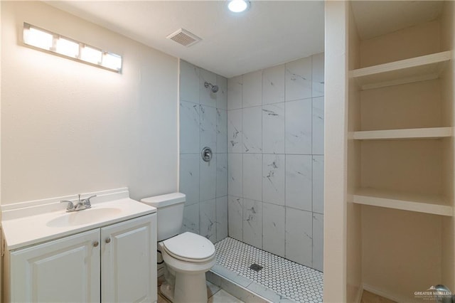 bathroom with visible vents, vanity, toilet, and tiled shower