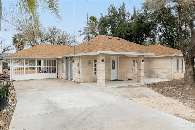 ranch-style house with concrete driveway, brick siding, roof with shingles, and a sunroom