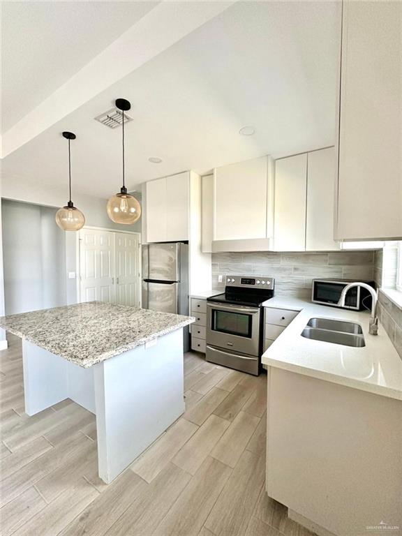 kitchen with stainless steel appliances, a kitchen island, sink, decorative light fixtures, and white cabinetry