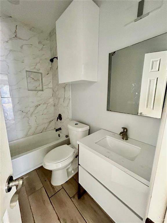 full bathroom with toilet, hardwood / wood-style floors, vanity, and tiled shower / bath combo