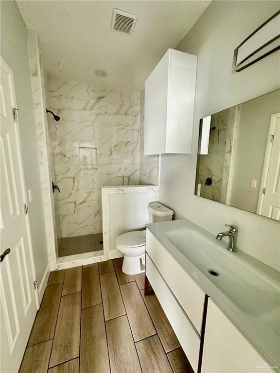 bathroom with vanity, toilet, and tiled shower