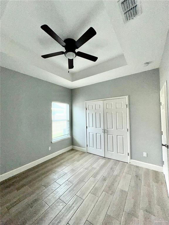 unfurnished bedroom with a raised ceiling, ceiling fan, a textured ceiling, light hardwood / wood-style floors, and a closet