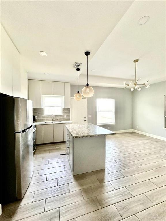 kitchen featuring sink, decorative light fixtures, white cabinetry, a center island, and stainless steel refrigerator