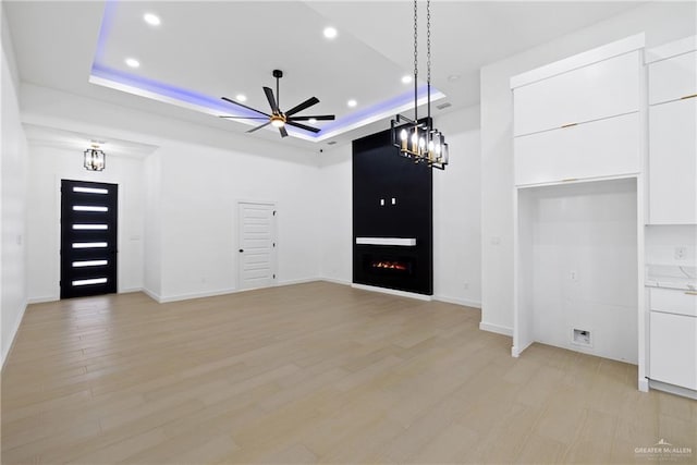 unfurnished living room featuring light wood-type flooring, a lit fireplace, a tray ceiling, and a ceiling fan