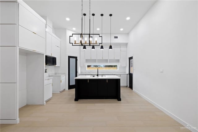 kitchen with white cabinets, an island with sink, hanging light fixtures, light countertops, and light wood-type flooring