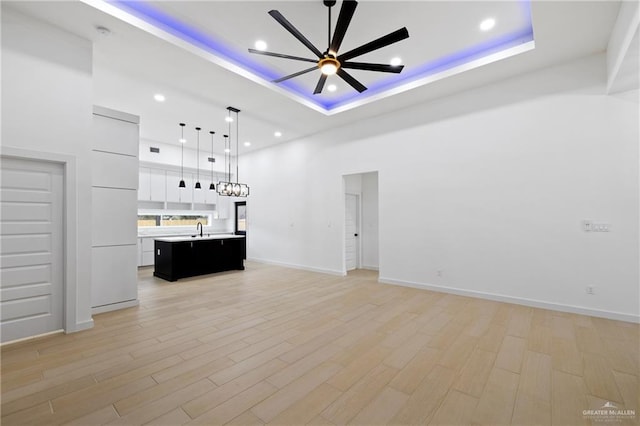 unfurnished living room with light wood-style floors, a high ceiling, a tray ceiling, and a ceiling fan