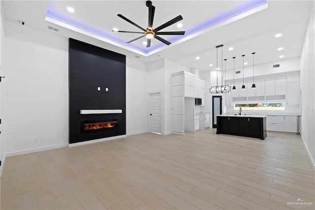 unfurnished living room with a large fireplace, a high ceiling, visible vents, a ceiling fan, and a raised ceiling