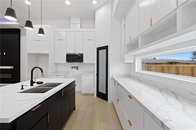 kitchen featuring light wood-style flooring, white cabinetry, a sink, light stone countertops, and dark cabinetry