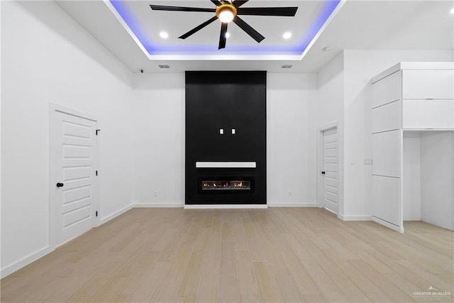 interior space featuring a fireplace, recessed lighting, a raised ceiling, light wood-style flooring, and a high ceiling