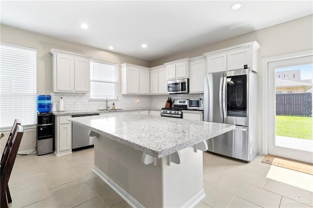 kitchen featuring tasteful backsplash, a kitchen island, light stone counters, white cabinets, and stainless steel appliances