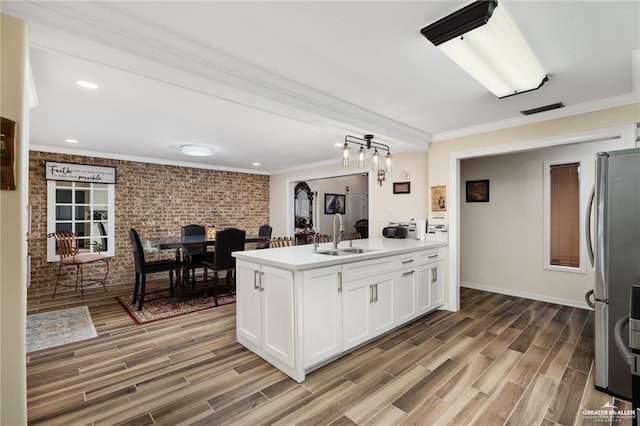 kitchen featuring brick wall, wood finish floors, a sink, and freestanding refrigerator