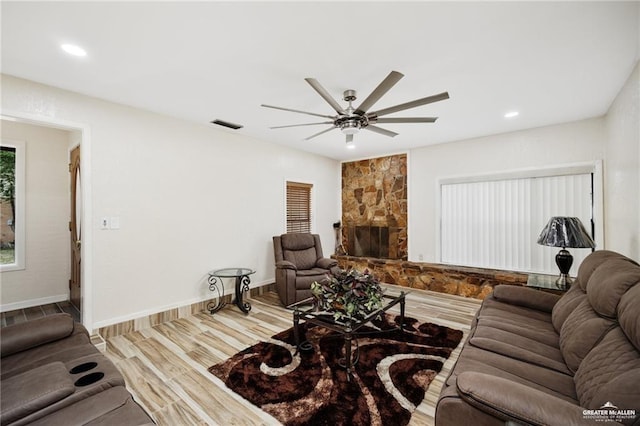 living area with ceiling fan, visible vents, wood finished floors, and a stone fireplace