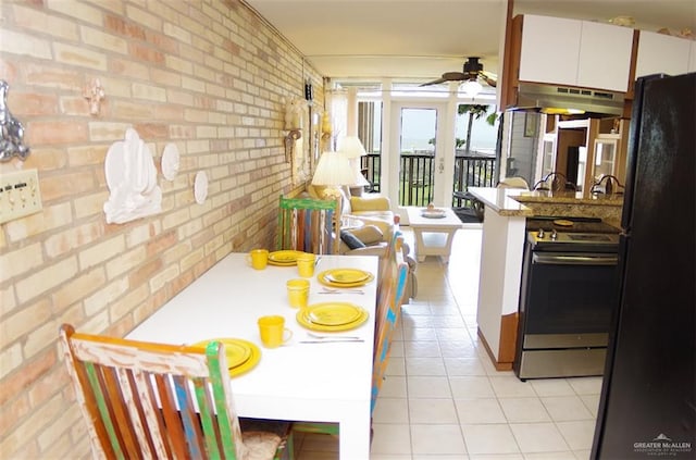 kitchen with under cabinet range hood, a ceiling fan, freestanding refrigerator, stainless steel electric stove, and brick wall