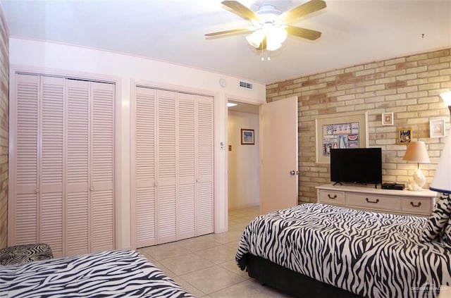 bedroom featuring light tile patterned flooring, visible vents, brick wall, a ceiling fan, and multiple closets