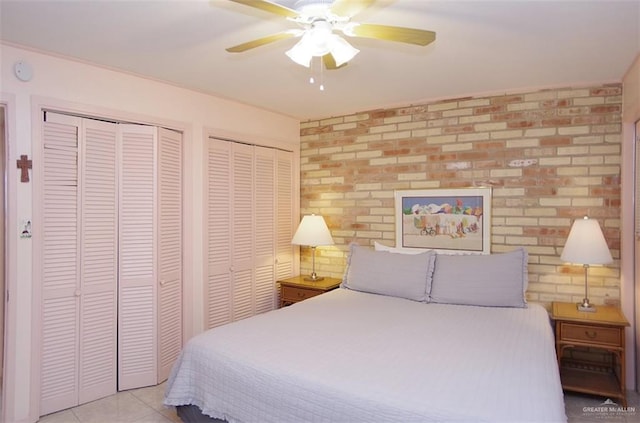 bedroom with brick wall, a ceiling fan, two closets, and tile patterned floors