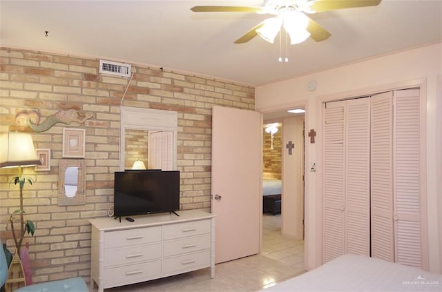 bedroom featuring visible vents, brick wall, a ceiling fan, a closet, and light tile patterned floors