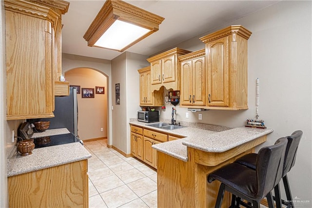 kitchen with a kitchen breakfast bar, arched walkways, appliances with stainless steel finishes, a sink, and a peninsula