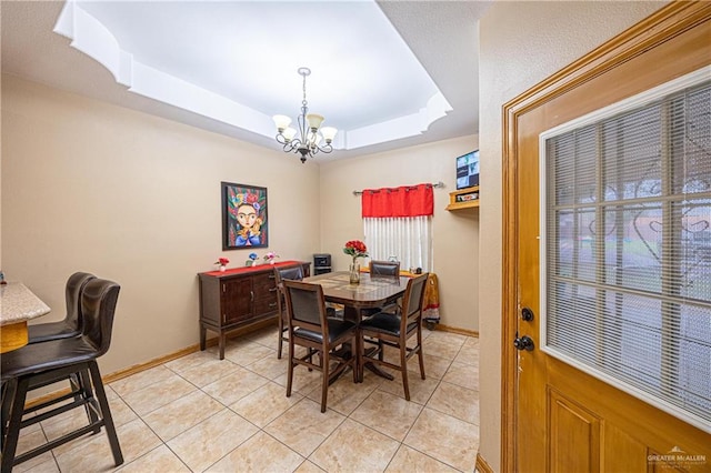 dining area with light tile patterned floors, baseboards, a tray ceiling, and a chandelier