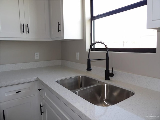 interior details with light stone countertops, sink, and white cabinets