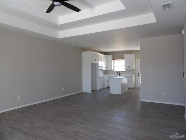 unfurnished living room featuring ceiling fan, dark hardwood / wood-style flooring, and a raised ceiling