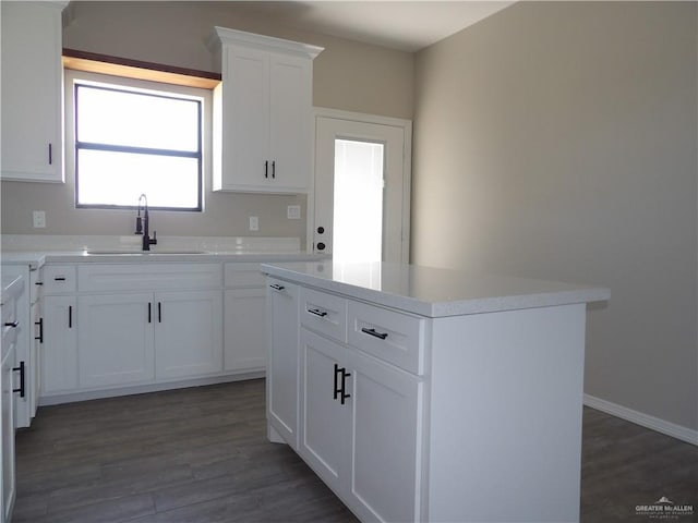 kitchen with dark wood-type flooring, sink, white cabinetry, and a kitchen island