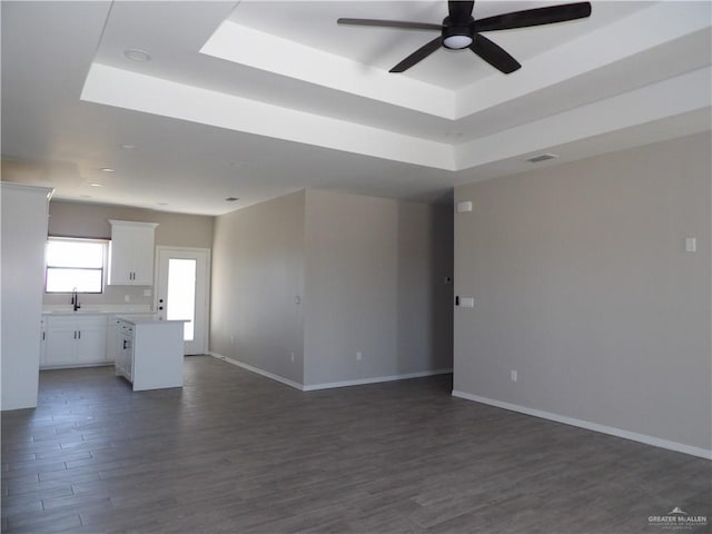 unfurnished living room with ceiling fan, dark wood-type flooring, sink, and a tray ceiling