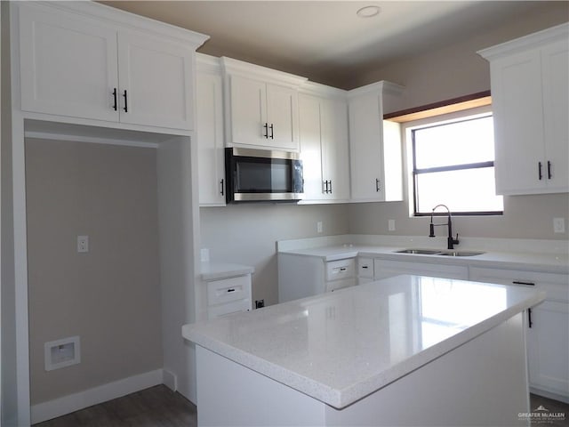 kitchen with dark wood-type flooring, a kitchen island, white cabinets, light stone counters, and sink