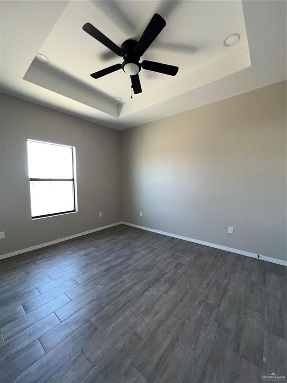 unfurnished room with ceiling fan, dark hardwood / wood-style flooring, and a tray ceiling