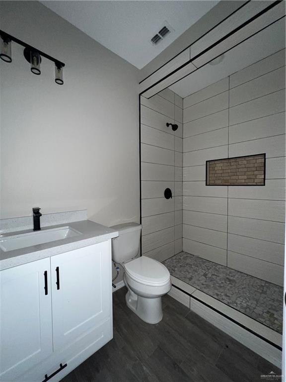 bathroom featuring hardwood / wood-style flooring, toilet, vanity, and a tile shower