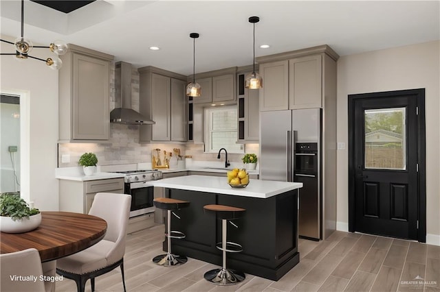 kitchen featuring high quality fridge, gray cabinets, decorative backsplash, wall chimney exhaust hood, and range with gas cooktop