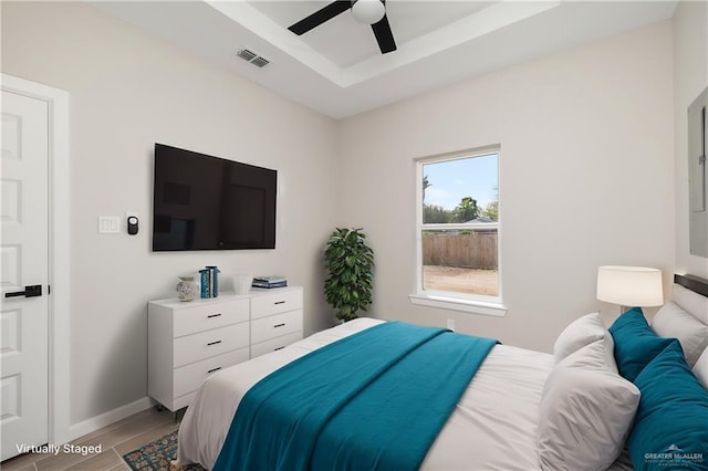 bedroom featuring visible vents, a raised ceiling, baseboards, ceiling fan, and light wood-style flooring