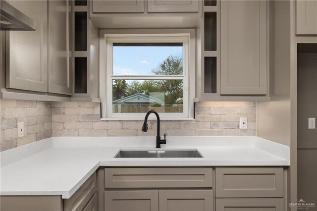 kitchen featuring gray cabinetry, a sink, light countertops, wall chimney range hood, and backsplash