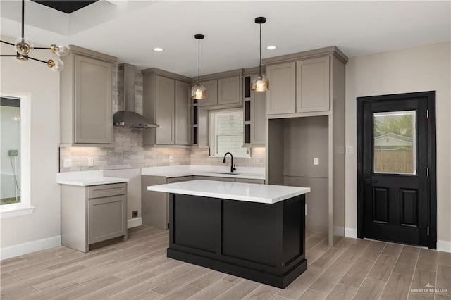 kitchen with a sink, gray cabinets, wood tiled floor, wall chimney exhaust hood, and tasteful backsplash