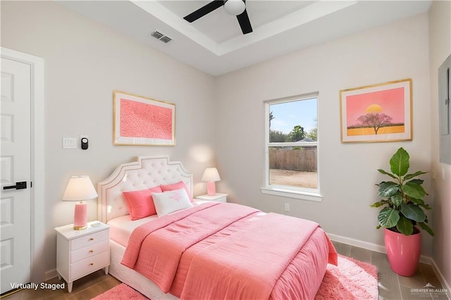 bedroom with ceiling fan, wood finished floors, visible vents, baseboards, and a raised ceiling