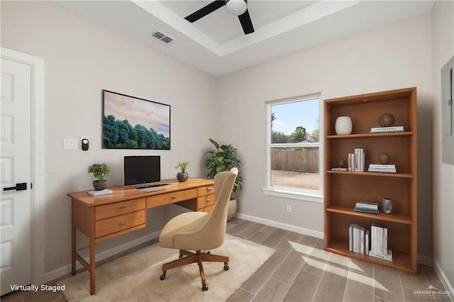 office space with wood finish floors, a tray ceiling, visible vents, ceiling fan, and baseboards