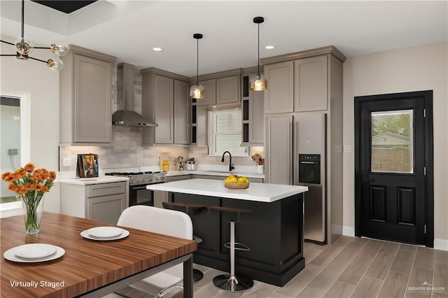 kitchen with tasteful backsplash, gray cabinets, stainless steel range with gas stovetop, fridge with ice dispenser, and wall chimney range hood