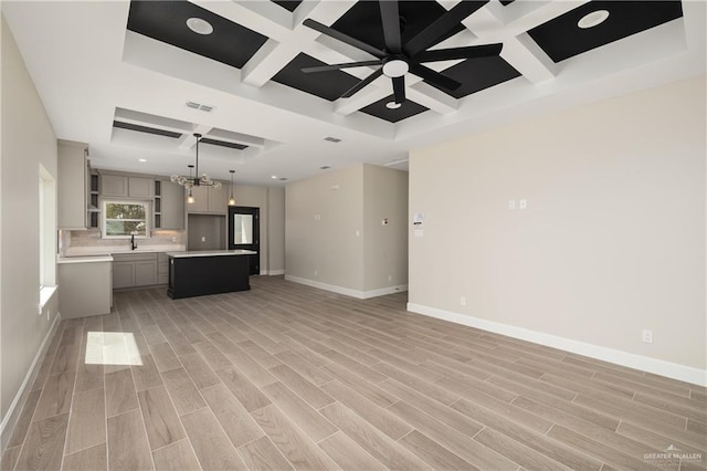 unfurnished living room featuring visible vents, light wood-style floors, a sink, coffered ceiling, and baseboards