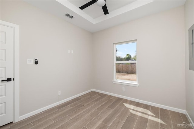 unfurnished room featuring visible vents, a raised ceiling, a ceiling fan, baseboards, and wood tiled floor