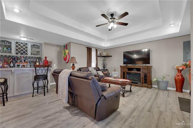 living room featuring a raised ceiling, ceiling fan, light hardwood / wood-style flooring, electric panel, and bar