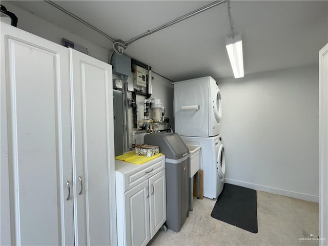 clothes washing area with cabinet space, baseboards, and stacked washer and clothes dryer