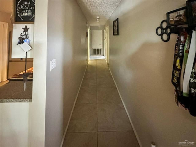 corridor featuring dark tile patterned floors, visible vents, a textured ceiling, and baseboards