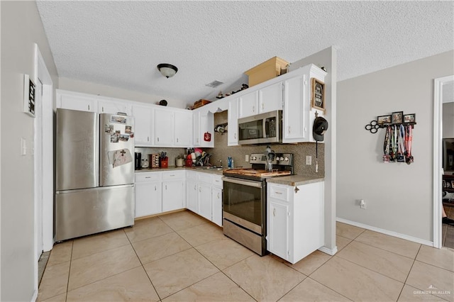 kitchen with tasteful backsplash, light tile patterned floors, white cabinets, and appliances with stainless steel finishes