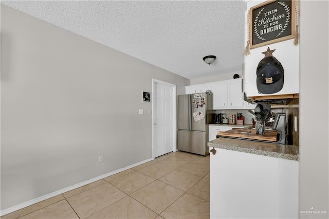 kitchen featuring tasteful backsplash, light tile patterned floors, freestanding refrigerator, a textured ceiling, and white cabinetry