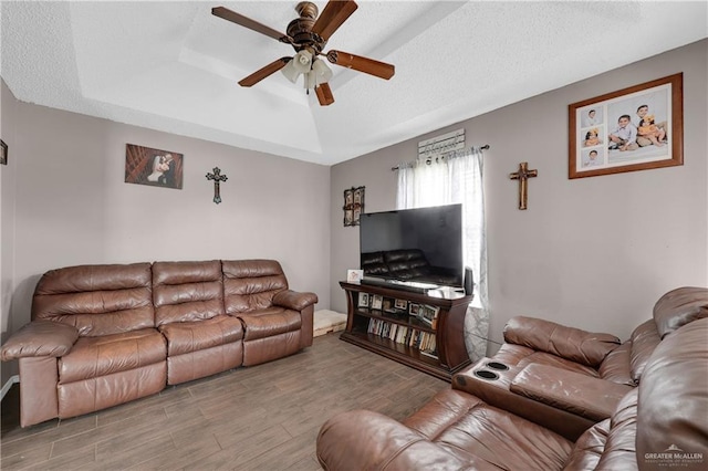 living area with a tray ceiling, a ceiling fan, wood finished floors, and a textured ceiling