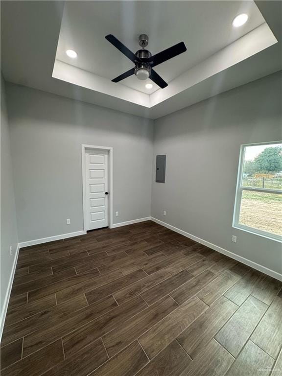 spare room featuring a raised ceiling, a ceiling fan, baseboards, and wood finish floors