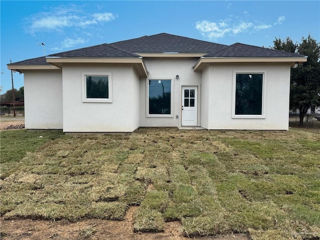 back of property featuring a yard, roof with shingles, and stucco siding