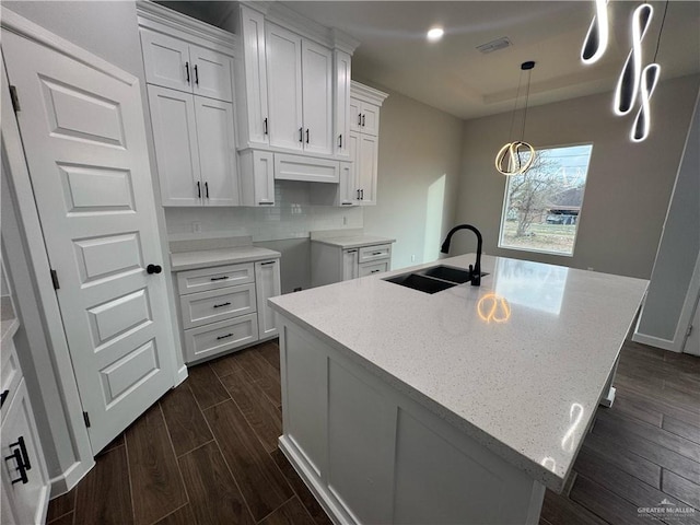 kitchen with light stone countertops, visible vents, wood tiled floor, a sink, and white cabinets