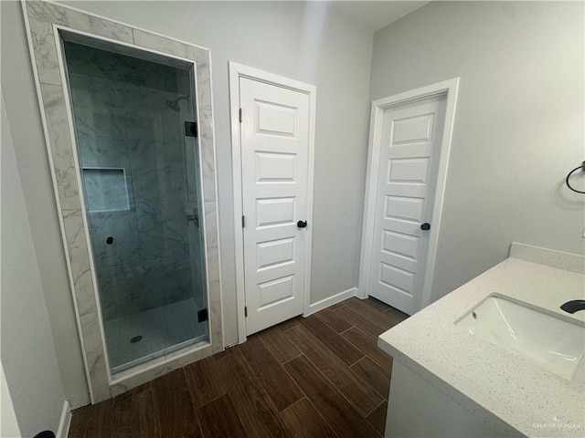 full bath featuring wood finish floors, a marble finish shower, baseboards, and vanity